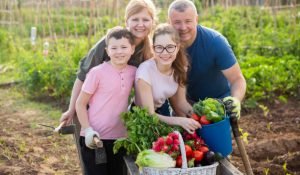Portrait of couple with boy and teen girl posing with fresh harvest on small agricultural family farm